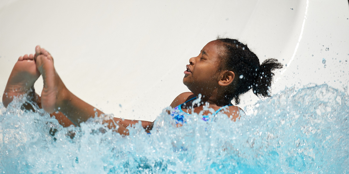 young African American girl landing in pool at the bottom of the water slide